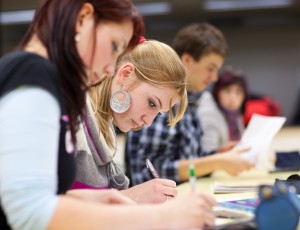 pretty female college student sitting in a classroom full of students during class (shallow DOF; color toned image)