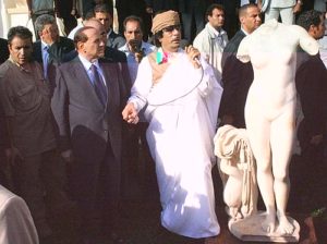 Libyan leader Moamer Kadhafi (C) holds the hand of Italian Prime Minister Silvio Berlusconi as he speaks with a microphone in his hand next to a Roman statue of the goddess Venus in the eastern city of Benghazi on Libya's Mediterranean coast on August 30, 2008. Berlusconi apologised to Libya for damage inflicted by Italy during the colonial era and signed a five-billion-dollar investment deal by way of compensation. Italy also returned to Libya the statue, dating back to the second century, which was found in 1913 by Italian troops near the ruins of the Greek and Roman settlement of Cyrene, on the Libyan coast. Berlusconi's visit to Benghazi 1,000 kms (650 miles) east of Tripoli coincides with the anniversary of the coup that brought Kadhafi to power on September 1, 1969.  AFP PHOTO/MAHMUD TURKIA